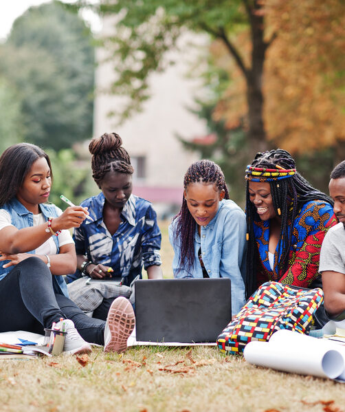 African college student Group of five african college students spending time together on campus at university yard. Black afro friends sitting on grass and studying with laptops.